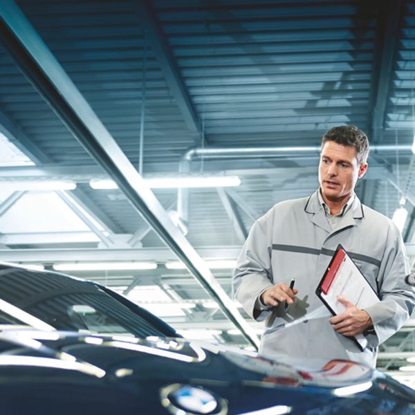 a technician with a clipboard in hand looking at a bmw car